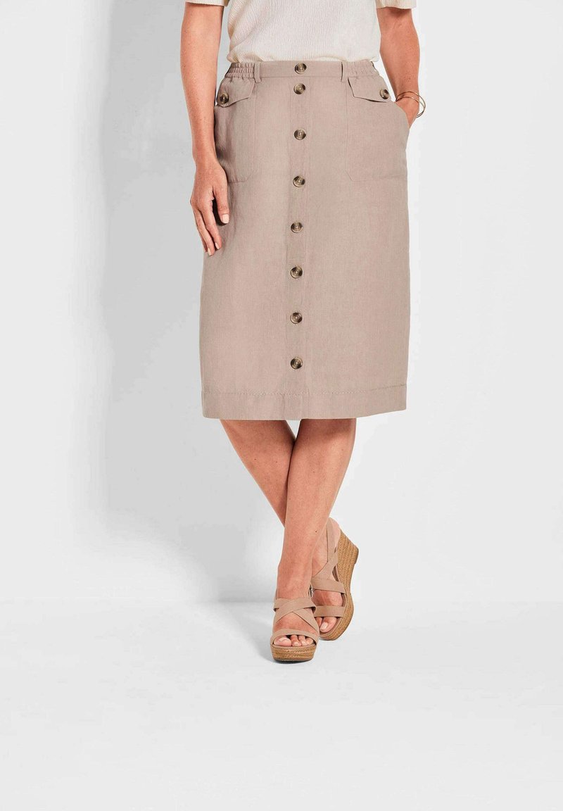 Beige Leinenrock in knieumspielender Länge mit vorderem Knopfverschluss, zwei vorderen Taschen und flachem Bund. Getragen mit hellbraunen Wedge-Sandalen.