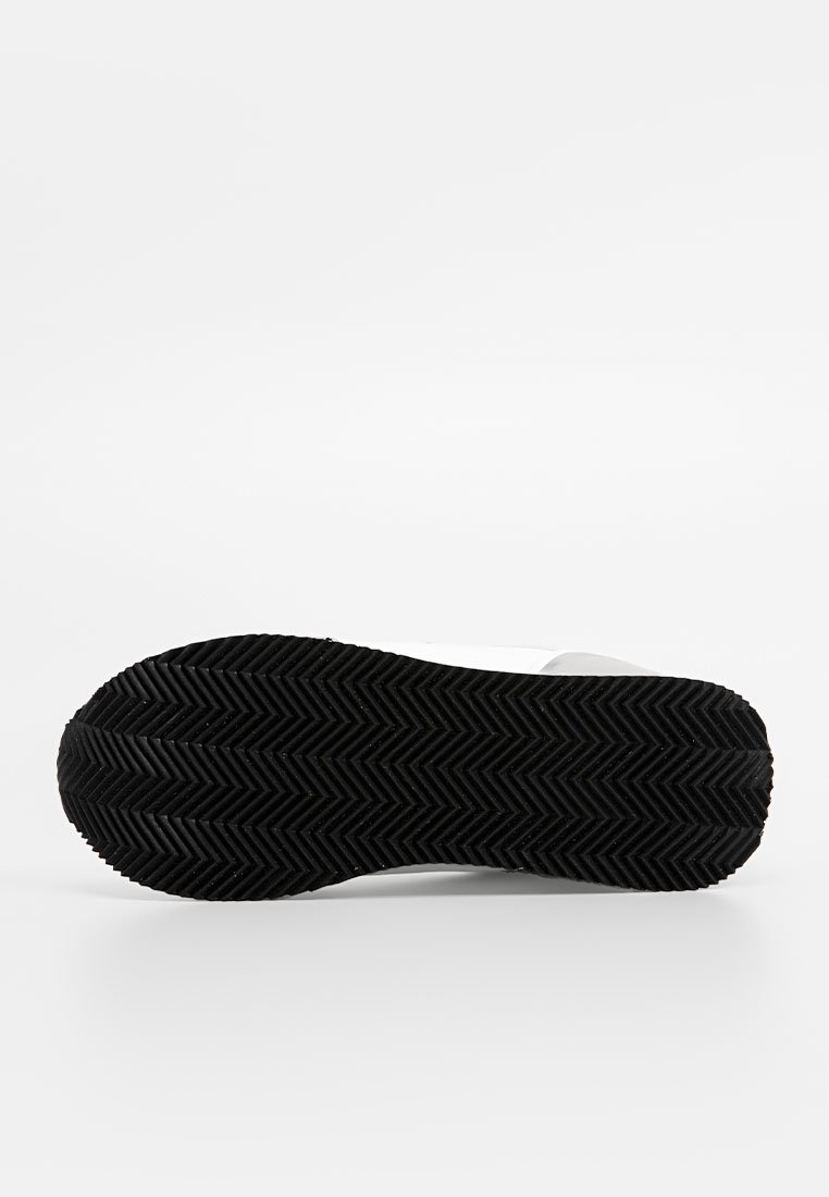 Semelle extérieure en caoutchouc noir avec un motif en chevrons, arborant un dessus blanc avec une texture lisse et un design minimaliste.