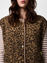 Woman wearing brown and black textured leopard print vest over beige and white striped shirt, front view from shoulders to lips.