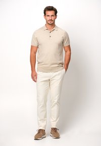 Beige stickad polo med korta ärmar, treknapps stängning; matchad med vita byxor och bruna sneakers. Enkel, åtsittande design.