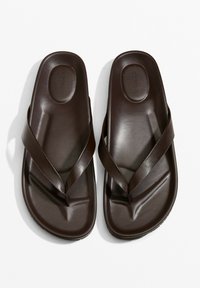 Barna, sima anyagból készült papucs, keresztpántos kialakítással. A talpak enyhén formázottak a kényelem és a tapadás érdekében.