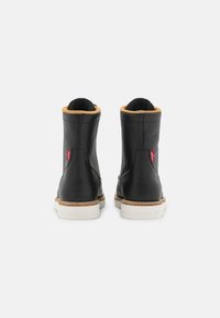 Botas de cuero negro hasta el tobillo con forro marrón claro, suela blanca y acentos de logo rojo. Cuentan con punta redonda y textura suave.