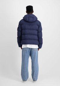 Chaqueta de plumas azul marino con capucha, presenta un diseño acolchado, puños elásticos y un ajuste holgado. Combinada con unos vaqueros ajustados de color azul claro.