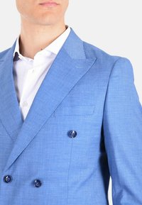 Blazer doppiopetto azzurro chiaro con rever a punta, tessuto texture, due bottoni scuri e taschino sul petto, abbinato a una camicia bianca.