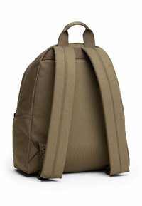 Mochila de tela marrón con dos correas anchas, un asa superior y un bolsillo lateral. Superficie texturizada y diseño minimalista.