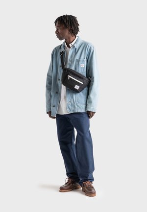 Casual outfit featuring a light blue denim jacket, white shirt, dark blue pants, and brown shoes; includes a black crossbody bag with zippers.
