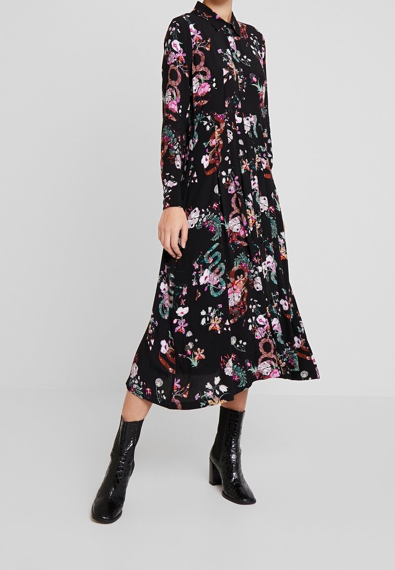 Robe maxi noire à fleurs avec manches longues, col à revers, et motifs colorés. Le tissu semble léger avec une texture lisse.