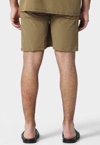 Shorts couleur khaki en tissu léger, avec une coupe droite, des bords ourlés et portés avec des sandales noires à enfiler.