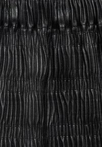 Tessuto in pelle nera con pieghe verticali, che mostra una superficie testurizzata con una leggera lucentezza e profondità creata dal design arricciato.