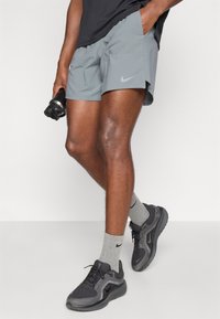 Γκρι αθλητικά σορτς με πλαϊνές τσέπες και διακριτό λογότυπο. Συνδυασμένα με γκρι κάλτσες και μαύρα αθλητικά παπούτσια με πλέγμα και υφές.