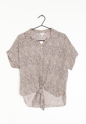 Short-sleeve beige blouse with black irregular dot pattern, front buttons, collar, and a front tie knot, hanging on a black hanger.