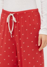 Pantalons rouges à cordon de serrage en tissu léger avec un motif de petits nœuds répété en crème. Taille élastique pour plus de confort.