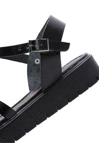 Sandales à plateforme noires en matériau brillant. Dotées de fines brides avec une boucle, d'une semelle texturée et d'une plateforme robuste avec des détails de crans.
