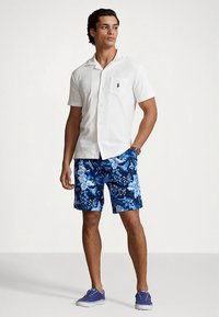 Λευκό πουκάμισο με κοντά μανίκια και τσέπη, μπλε floral σορτς και μπλε καμβά παπούτσια. Ύφασμα λείο με άνετη εφαρμογή, με κλασικό γιακά.