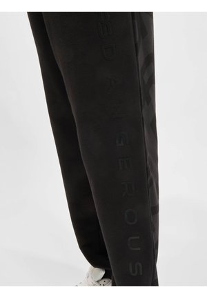 Black sweatpants made of soft material featuring a tonal logo design along the side, with a tapered fit and elastic waistband.
