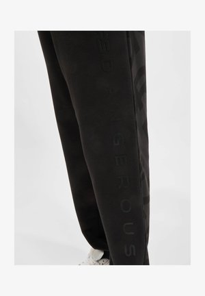 Black sweatpants made of soft material featuring a tonal logo design along the side, with a tapered fit and elastic waistband.