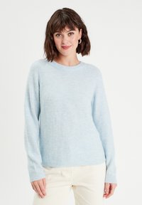 Suéter azul claro con una textura suave y esponjosa, cuello redondo y mangas largas. Diseño minimalista, sin patrones ni herrajes visibles.
