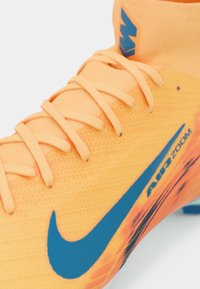 Baskets Nike orange vif avec une tige texturée, présentant des accents bleus, des lacets et le logo "AIR ZOOM". Conçues pour la performance athlétique.