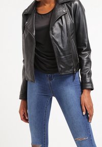 Czarna skórzana kurtka motocyklowa z srebrnymi elementami, zamykanymi kieszeniami i dopasowanym krojem. Zestawiona z niebieskimi, podartymi rurkami.
