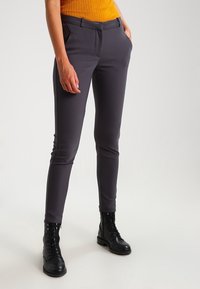 Pantaloni grigi aderenti con tasche frontali, realizzati in morbido tessuto elasticizzato. Abbinati a un maglione a coste giallo senape e stivali neri con lacci.