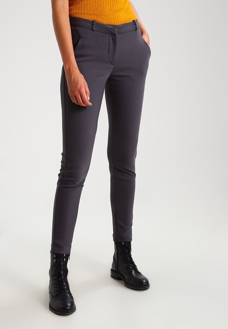 Grijze aangesloten broek met zijzakken, gemaakt van soepele stretchstof. Gecombineerd met een geribde mosterdkleurige trui en zwarte veterschoenen.