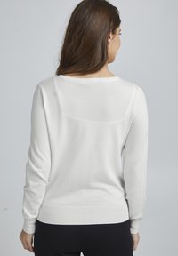 Maglione bianco con maniche lunghe, orlo a coste e dettaglio del pannello posteriore, realizzato in tessuto morbido. Vista da dietro, capelli che cadono lungo la schiena.