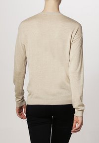 Beige knit sweater with long sleeves, ribbed hem, and crew neckline. Soft texture and relaxed fit. No distinct patterns.