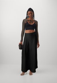Jupe maxi en satin noir associée à un top noir court avec un design à manches longues pailletées et un lien au niveau du col.