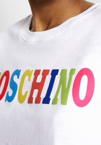 Camiseta blanca con letras audaces y multicolores que dicen "MOSCHINO" en rojo, azul, verde, amarillo y rosa. Tejido suave con un cuello redondo clásico.