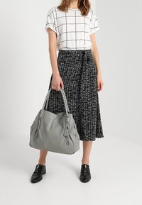 Szara skórzana torebka z dwiema okrągłymi uchwytami, z zamkami błyskawicznymi i metką. Stylizacja obejmuje biały top w kratkę oraz czarną spódnicę w wzory.