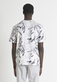 Camiseta de manga corta en algodón blanco mezclado con estampado de hojas negras. Cuenta con un cuello redondo y un corte relajado, asegurando comodidad y transpirabilidad.