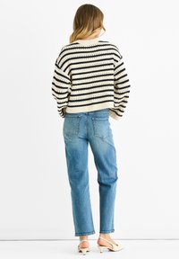 Knit sweater with black and cream horizontal stripes, loose fit, round neckline, paired with blue high-waisted jeans and light-colored slingback shoes.