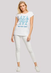 White cotton t-shirt featuring a blue graphic of three fish and the text "SALTY BUT SWEET" below. Paired with white skinny jeans and sneakers.