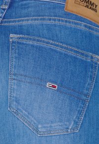 Los jeans de mezclilla azul cuentan con un bolsillo trasero con costuras en blanco y un pequeño logo bordado en rojo, blanco y azul.