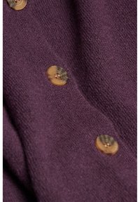Gros plan d’un tissu violet texturé avec trois boutons ronds couleur sable cousus en ligne verticale.