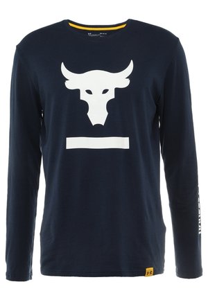 Chemise bleu marine à manches longues avec un grand logo blanc de tête de taureau et une barre horizontale sur le devant, petite étiquette jaune avec le logo Under Armour à l’ourlet.