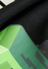 Schwarzer Stoff mit einem lebhaften grünen Grafikdesign. Das Material wirkt glatt mit Textilstruktur und zeigt geometrische Formen und Muster.