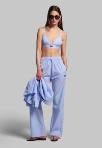 Raidallinen sininen vapaa-ajan asu koostuu kolmion muotoisesta bralette-topista ja väljästä housuista. Kangas on kevyt, pehmeätekstuurinen ja säädettävissä olevat olkaimet.