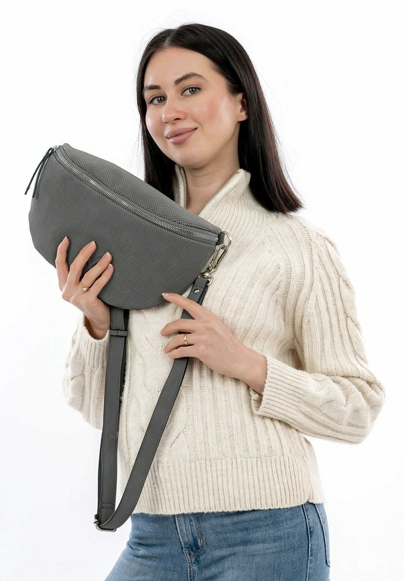 Borsa crossbody grigia e texture con chiusura a zip, tracolla regolabile e forma a mezzaluna, tenuta da una persona in un maglione crema.