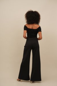 Crna off-shoulder majica u kombinaciji s crnim širokim hlačama visokog struka, izrađena od glatkog materijala s priljubljenim siluetom i minimalnim šavovima.