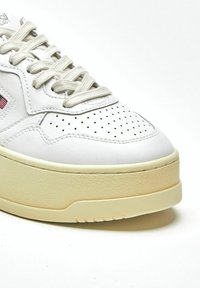 Sneaker in pelle bianca con dettagli traforati, chiusura con lacci e suola beige effetto texture. Caratteristiche includono punta rialzata e design minimale.