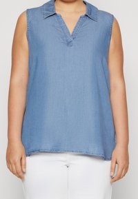 Lysblå ærmeløs top med krave, der har en v-halsudskæring og frynset kant. Lavet af stof, der ligner denim. Ingen synlige mønstre eller detaljer.