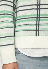 Gestreifter Pullover in hellgrün, grau und weiß. Mit einem gerippten Saum und weicher Textur, über einem weißen Hemd getragen.