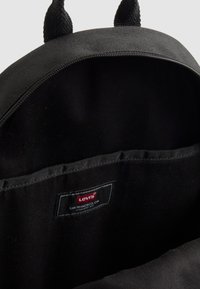 Svart stoff ryggsekk interiør med en Levi's etikett sydd inne i lommen, synlig glidelås, og to svarte bærehåndtak på toppen.