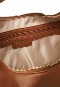 Interno di una borsa in pelle marrone con una zip dorata e un rivestimento in tessuto color crema con un logo. Texture liscia e design semplice.