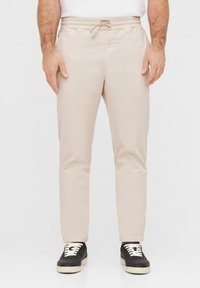 Beige, leichte Hose mit elastischem Bund und Kordelzug. Gerades Bein-Design, kombiniert mit schwarzen Sneakers mit weißen Schnürsenkeln.