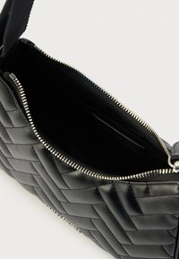 Μαύρη δερμάτινη τσάντα με καπιτονέ σχέδιο και φερμουάρ, με λεία υφή και εσωτερική τσέπη. Διαθέτει ασημένιες μεταλλικές λεπτομέρειες.