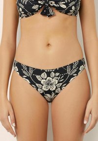 Chiloți negri cu un model floral în nuanțe de crem. Au un croi înalt pe picior și o talie lată pentru confort și stil.