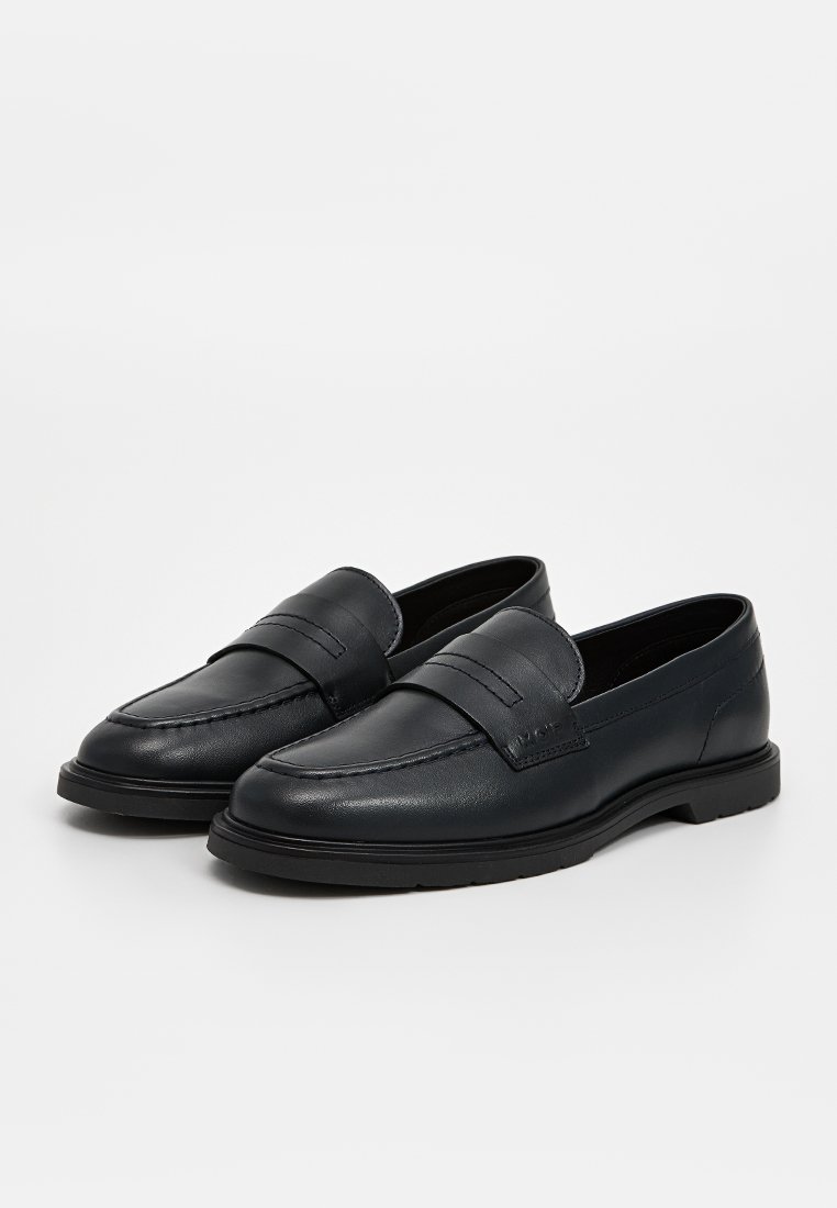 Mocassins en cuir noir avec une texture lisse, dotés d'une bande surélevée sur le dessus et d'une semelle en caoutchouc plate pour un confort optimal.