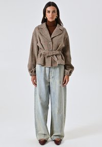 Giacca oversize a quadri con cintura, chiusura a bottoni e maniche lunghe, abbinata a jeans larghi in denim chiaro strappati e mocassini marroni.
